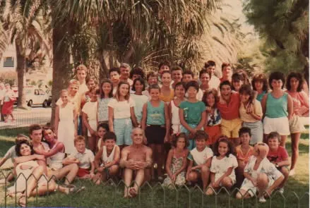 Gruppo di bambini e adulti in posa su un prato, con palme sullo sfondo.