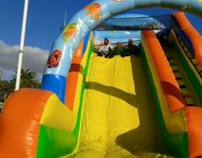 Scivolo gonfiabile colorato con decorazioni marine e bambini sulla piattaforma superiore.